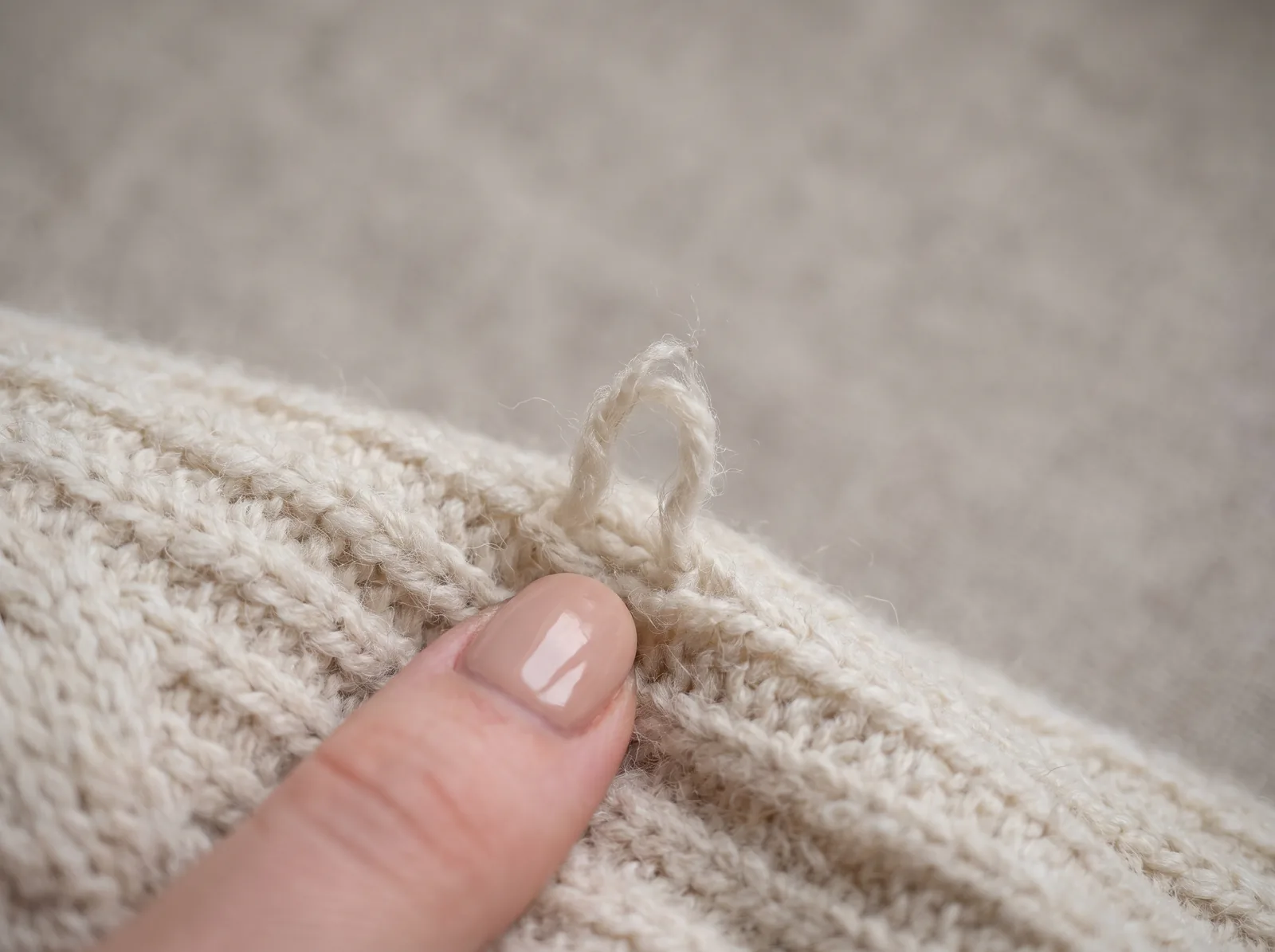 A fingertip pointing at a small pulled loop of yarn on a cream knit sweater