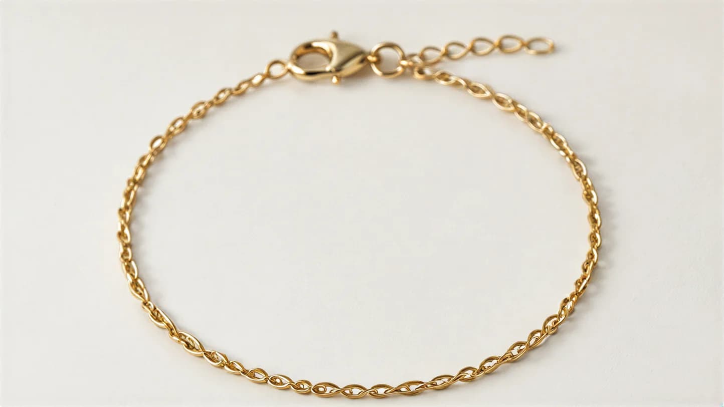 A fine gold chain bracelet with a lobster clasp and a short extender chain, laid in a circle on a plain off-white surface