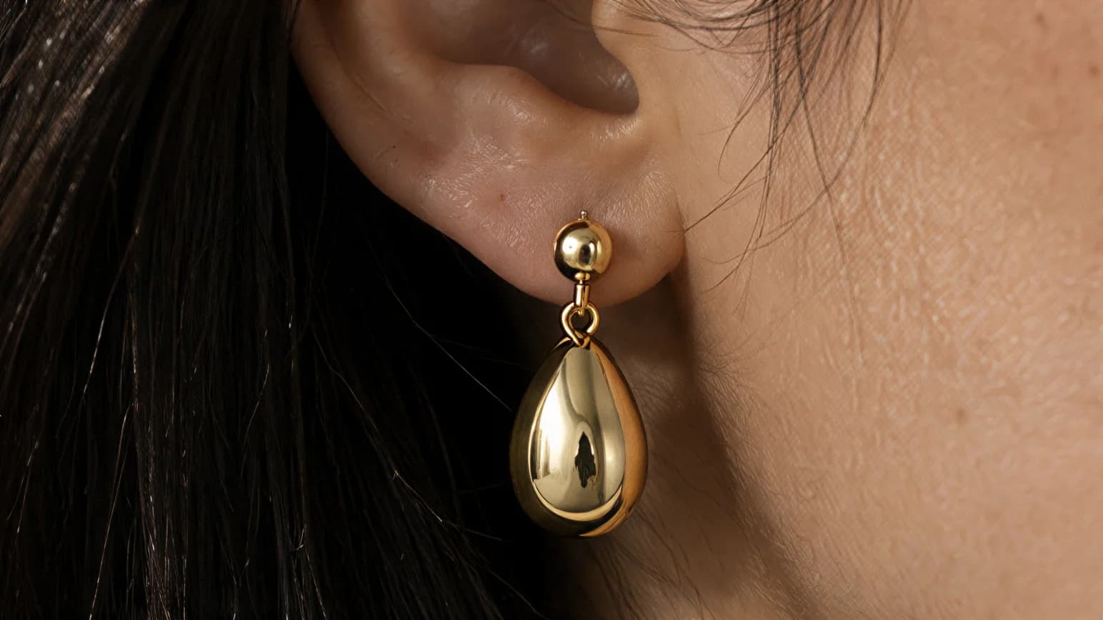 Macro close-up of the gold drop earring on the ear