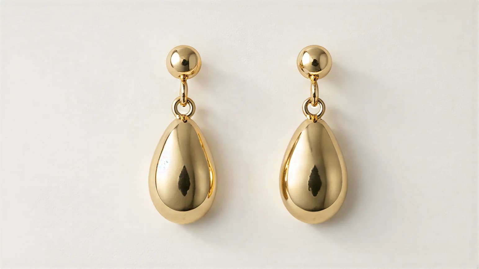 A pair of polished gold teardrop earrings on a plain white surface