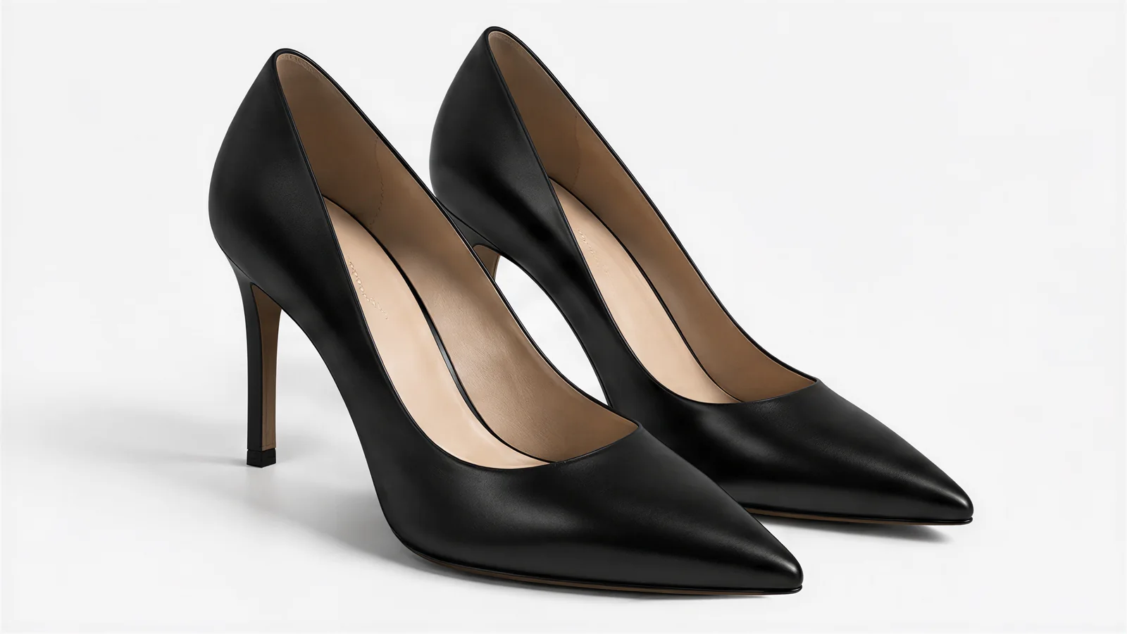 A pair of black leather pointed-toe pumps with thin stiletto heels on a white background