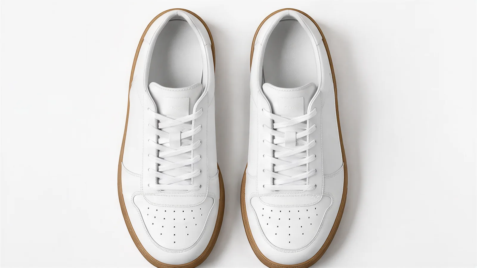 The pair of white sneakers with gum soles seen from directly above, showing the laces and insoles