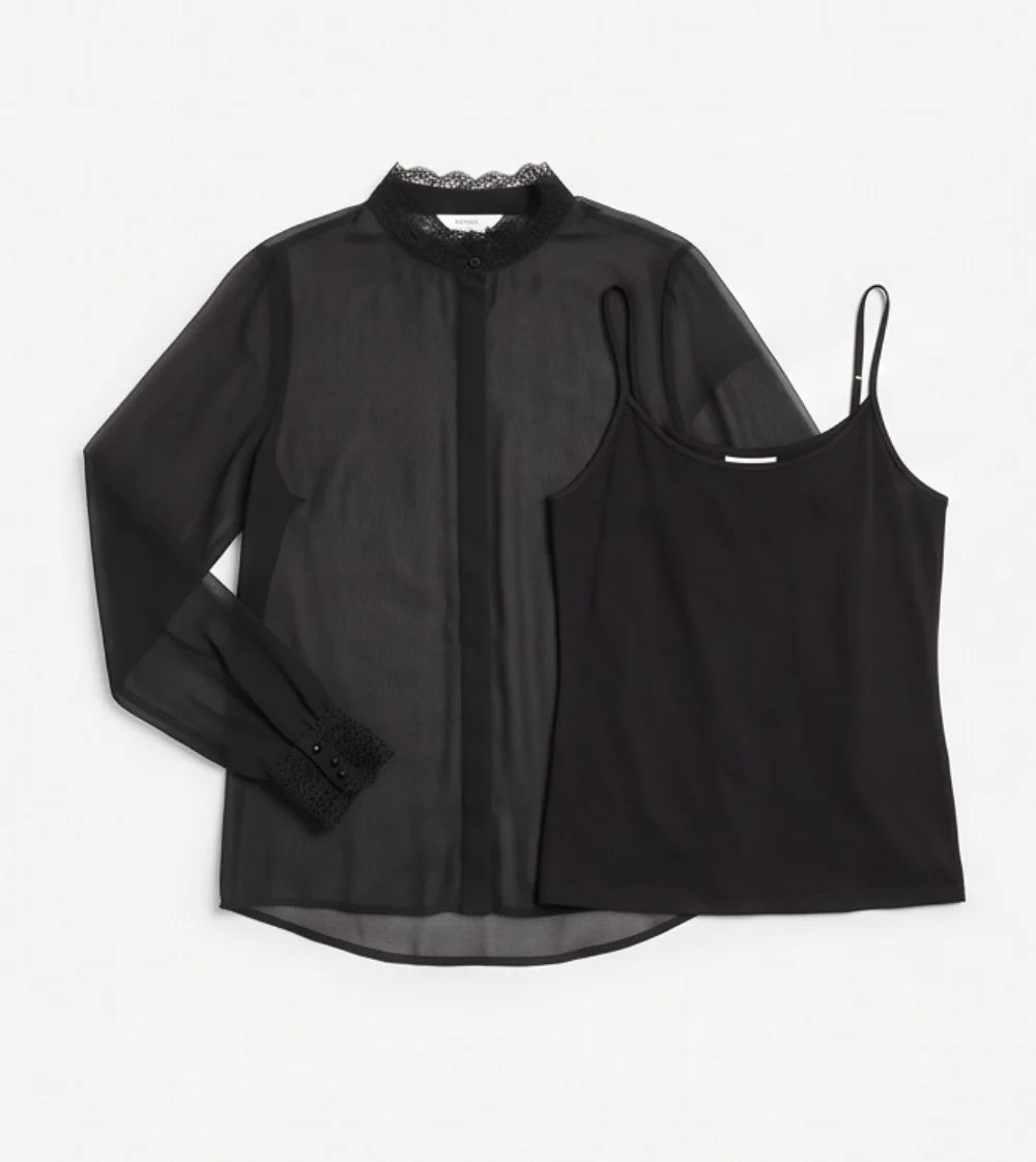 A sheer black chiffon blouse with a lace collar and lace cuffs laid flat beside a black camisole, on a pale gray background