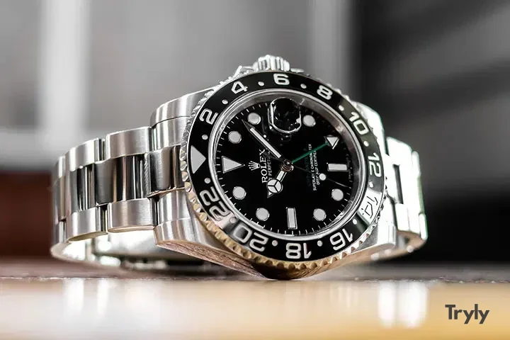 A steel dive-style watch with a black dial and bezel lying on its bracelet on a wooden table, shot at eye level