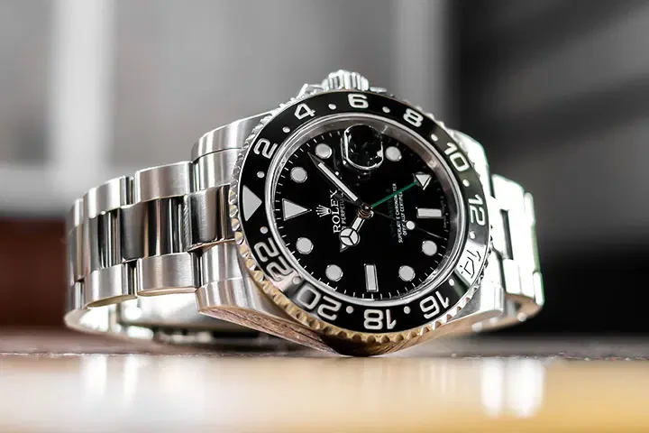 A steel dive-style watch with a black dial and bezel lying on its bracelet on a wooden table, shot at eye level
